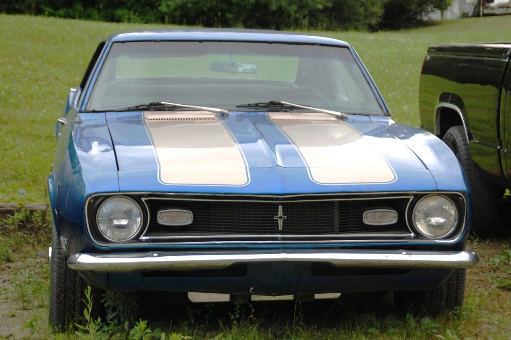 A blue classic car with racing stripes on the hood